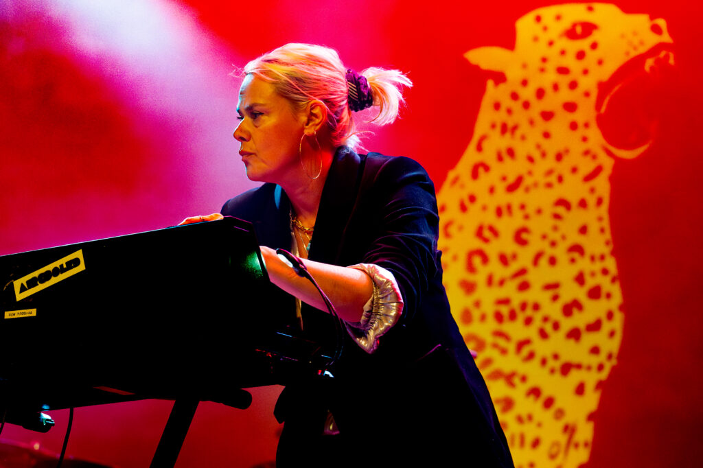 mew on stage playing keyboard in front of her leopard print backdrop